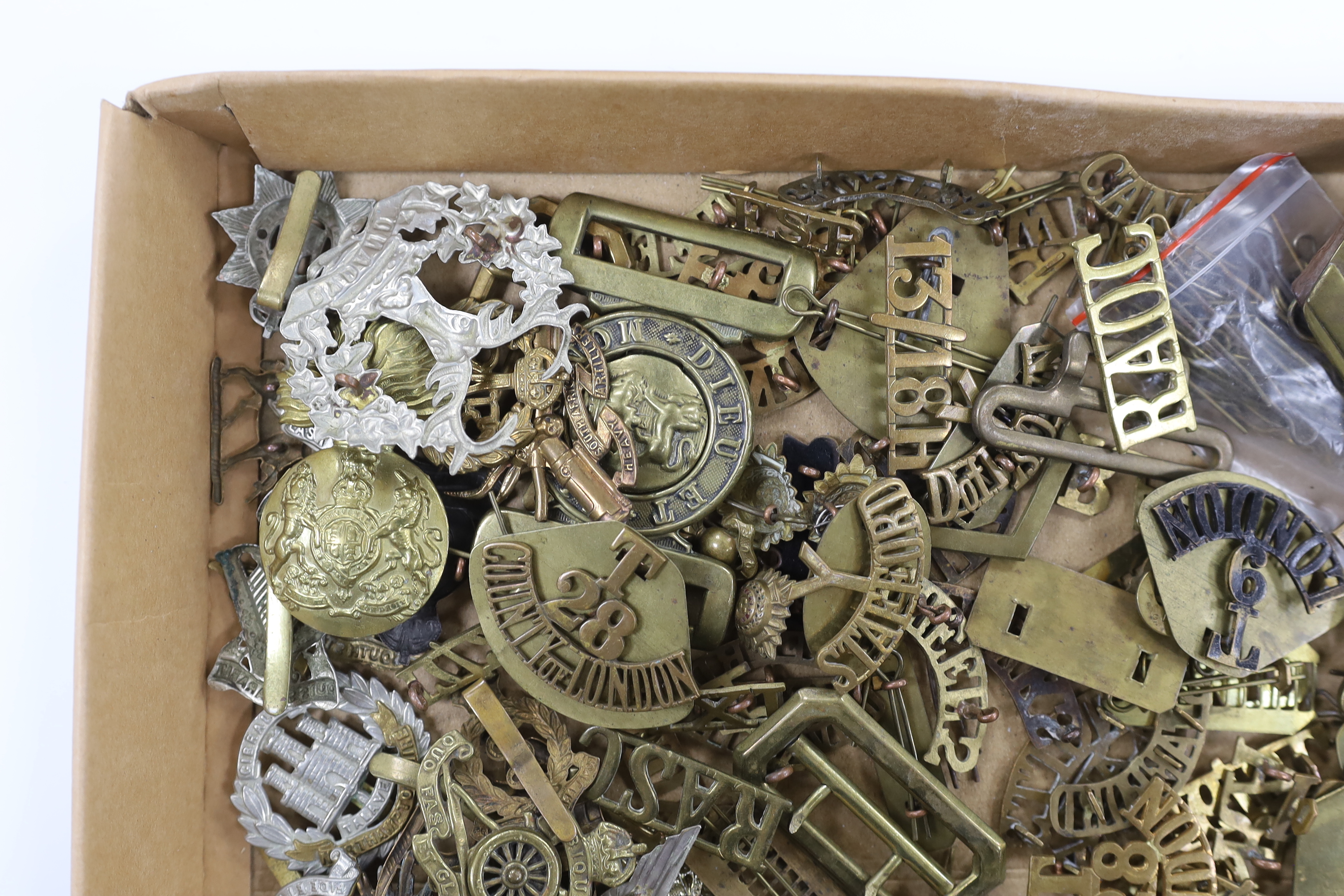 A collection of military cap badges, shoulder titles, pins, backing plates, belt buckles, etc.
